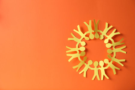 Paper figures of people holding hands on orange background, top view. Space for text
