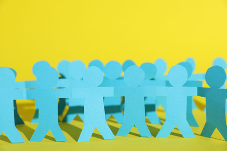 Human paper figures holding hands on yellow background, closeup