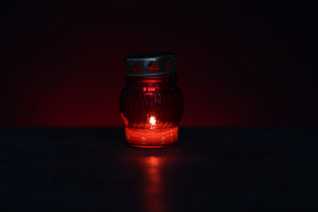 Grave lantern with burning candle on black table against red background