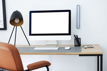 Stylish workplace with wooden desk, lamp and computer indoors. Mockup for design