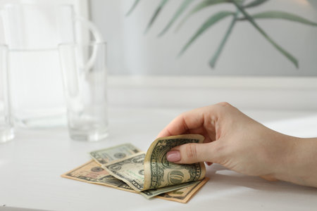 Woman taking tips from white wooden counter in hotel room, closeup. Gratuity for work