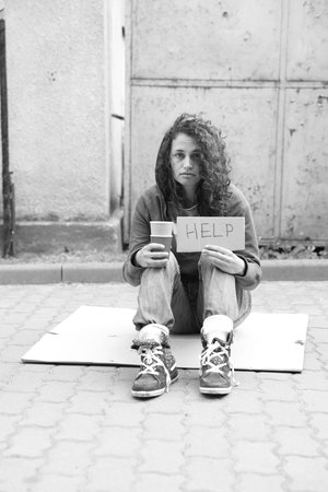 Homeless woman with sign Help and paper cups on cardboard outdoors. Black and white effect