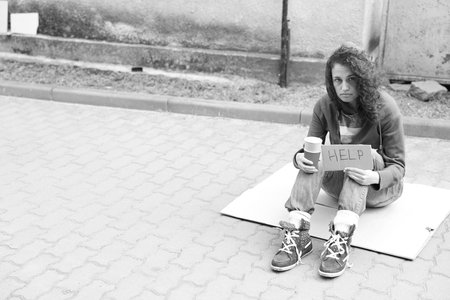 Homeless woman with sign Help and paper cups on cardton outdoors, space for text. Black and white...