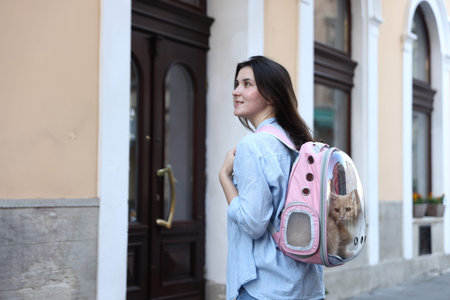 Woman with her cute cat in backpack carrier on city street. Space for textの写真素材