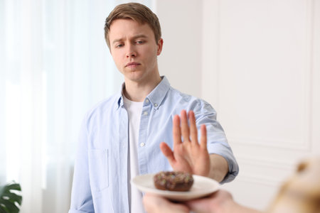 Gluten free diet. Man refusing from donut indoors, selective focus
