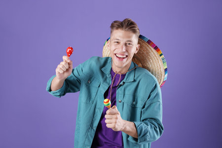 Happy man with sombrero hat playing maracas on purple background