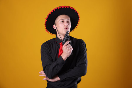 Man in black Flamenco hat with gun on yellow backgroundの写真素材