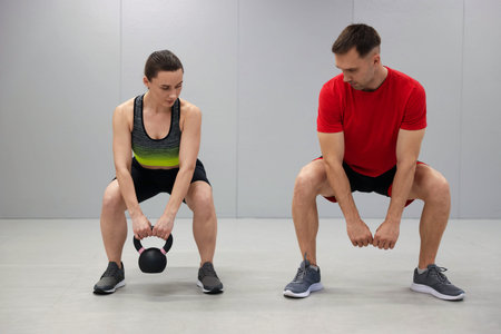 Young woman exercising with kettlebell with professional personal trainer in gym