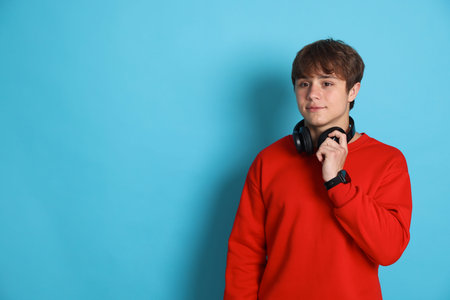 Teenage boy with headphones on light blue background. Space for text
