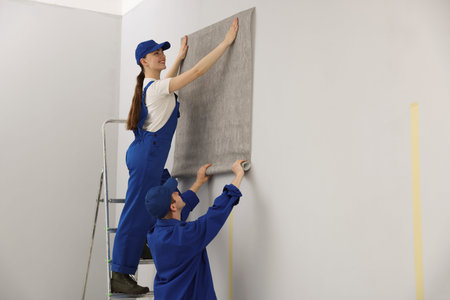 Workers putting wallpaper on wall in room. Space for text