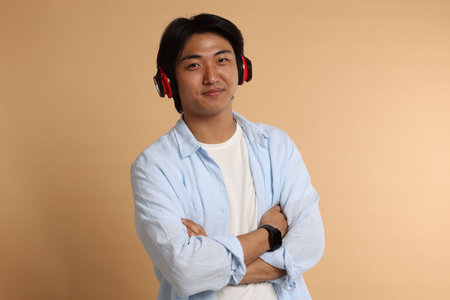 Handsome Asian man in headphones on beige background