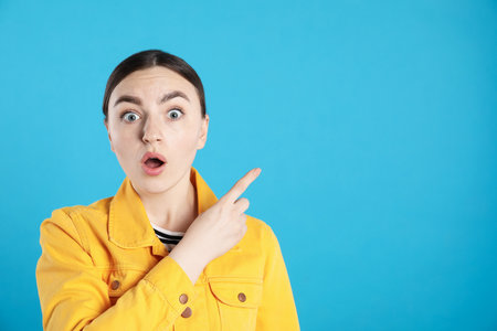 Surprised woman pointing at something on light blue background, space for textの写真素材