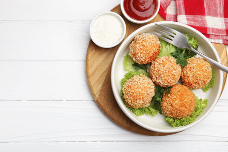 Delicious fried croquette balls with parsley, lettuce and sauces on white wooden table, top view....