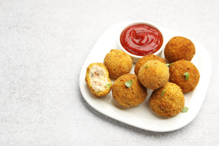 Delicious fried croquette balls with parsley and ketchup on gray textured table, closeup. Space for...