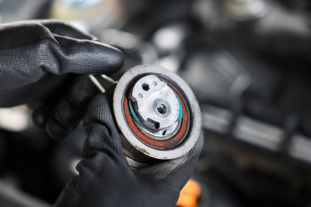 Auto part. Professional mechanic with idler-wheel near open hood of car indoors, closeup. Space for...