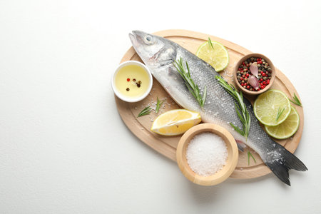 Fresh raw seabass fish with spices on white table, top view and space for text. Seafood delicacies