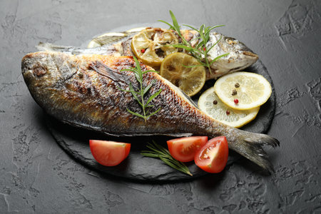 Tasty roasted dorado fish with spices and tomato on black table, closeup. Homemade seafood dish
