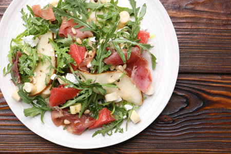 Tasty salad with arugula, prosciutto, cheese, pear, grapefruit and nuts on wooden table, top viewの写真素材