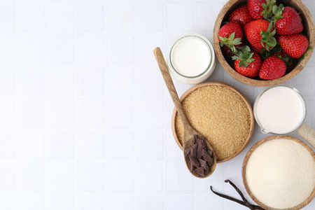 Different ingredients for panna cotta. Milk, sugar, vanilla, chocolate and strawberries on white tiled table, flat lay. Space for textの写真素材