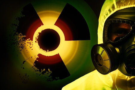 Man wearing hazmat suit and gas mask on dark background. Glowing radioactive sign behind himの写真素材
