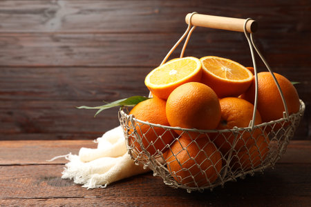 Fresh ripe oranges and leaves in basket on wooden table, closeup. Space for textの写真素材