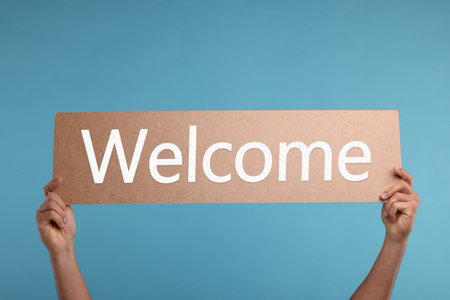 Man holding Welcome sign on light blue background, closeup