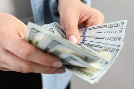 Woman counting dollar banknotes on light gray background, closeup