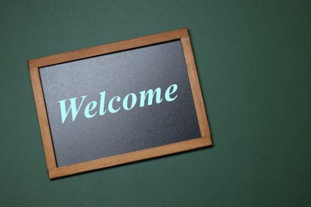Small chalkboard with word Welcome on green background, top view