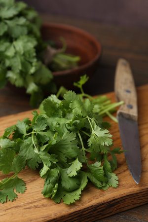 Cutting board with fresh cilantro and knife on wooden table, closeup