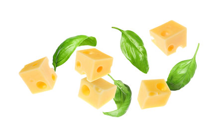 Cheese cubes and green basil leaves flying against white background