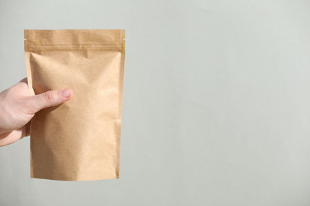 Woman holding blank zipper stand-up pouch on light grey background, closeup. Space for text