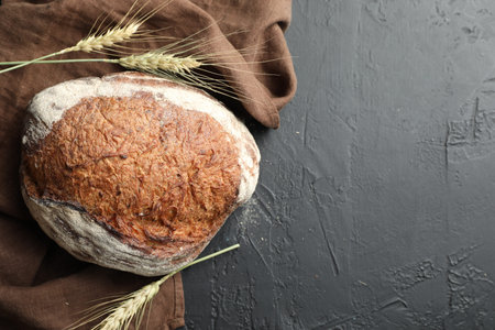 Loaf of fresh bread and spikes on black table, flat lay. Space for text