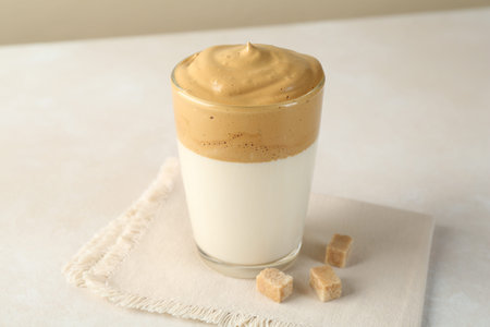 Delicious dalgona coffee in glass cup and brown sugar on light table, closeup