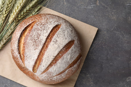 Fresh bread and green wheat spikes on gray table, flat lay. Space for text