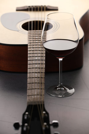 Acoustic guitar and red wine on grey table, closeup
