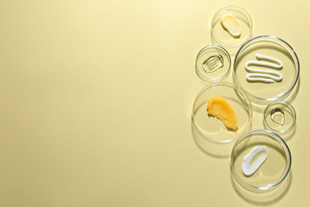 Different cosmetic products in Petri dishes on pale yellow background, flat lay. Space for textの写真素材