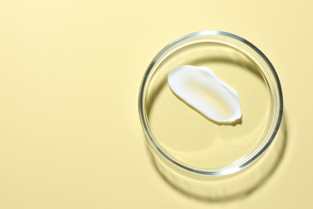 Cosmetic product in Petri dish on pale yellow background, top view. Space for textの写真素材