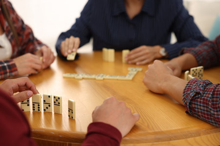 Friends playing dominoes at wooden table against light background, closeupの写真素材