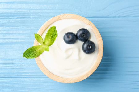 Tasty yoghurt with blueberries and mint in bowl on light blue wooden table, top viewの写真素材
