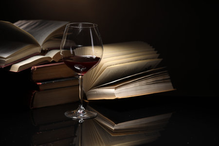 Red wine in glass and stack of books on mirror table against dark background, closeupの写真素材