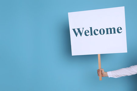 Woman holding Welcome sign on light blue background, closeup