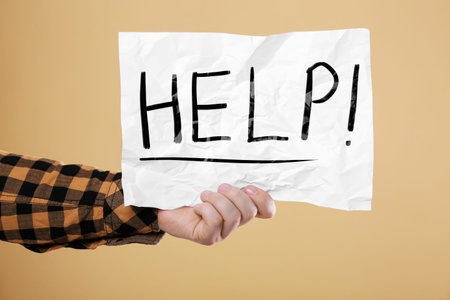 Man holding paper with word Help against pale orange background, closeup
