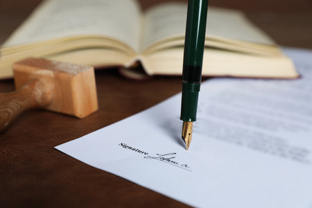 Signing notary document with fountain pen at leather surface against brown background, closeupの写真素材