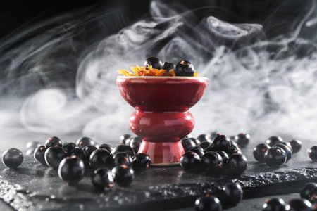 Hookah bowl with currants and smoke on black table, closeup