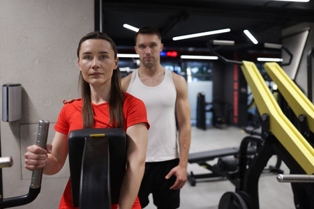 Young woman exercising on seated row machine with professional personal trainer in gym