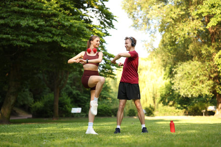 Happy couple in headphones doing morning exercises in park, low angle view