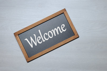 Small chalkboard with word Welcome on wooden background, top view