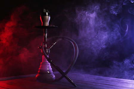 Hookah on wooden table with smoke in color lights against black backgroundの写真素材