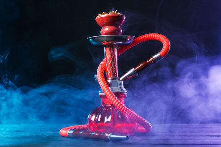 Hookah on wooden table with smoke in color lights against black background