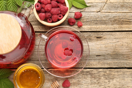 Tasty raspberry tea, berries and leaves on wooden table, flat lay. Space for text